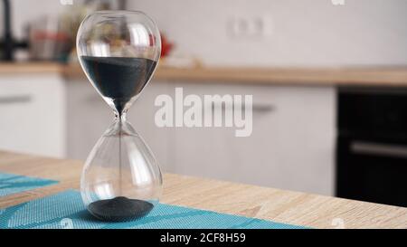 Closeup of hourglass on a white wooden table with defocus kitchen on background. Concept of time to cook. Stock Photo