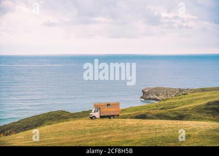 Golden field on hill and small cargo truck with blue sea and cloudy sky on background at Comillas Cantabria at Spain Stock Photo