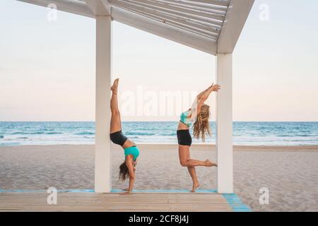 Inspired women making acroyoga first hollowback handstand on beach Stock Photo