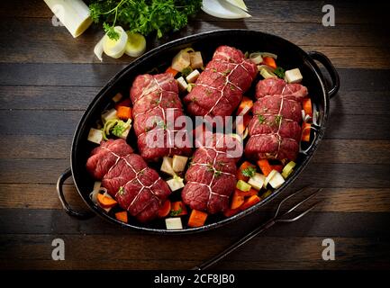 Preparing a traditional German meal of beef roulades in an oven dish with fresh vegetables and seasoning viewed top down on a kitchen table Stock Photo