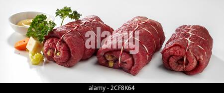 Row of three uncooked prepared beef roulades with parsley, mustard and fresh ingredients on white in a panorama banner Stock Photo