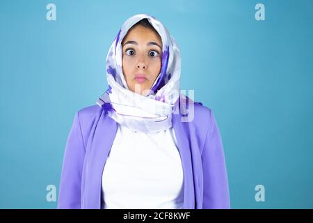 Young beautiful arab woman wearing islamic hijab over isolated blue background making fish face with lips, crazy and comical gesture. Stock Photo