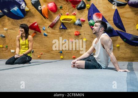 Side view of muscular smiling man and Woman sitting on floor and smiling away while having training in climbing gym Stock Photo