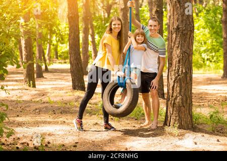 Parents pushing child daughter on tire swing in autumn park Stock Photo