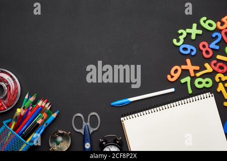 plastic multi-colored numbers, colorful wooden pencils, scissors, notepad on a blank black chalk board, school stationery, copy space Stock Photo