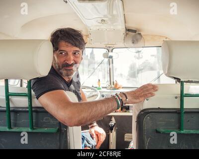 Smiling kind bearded man in front seat watching looking over shoulder in old car Stock Photo