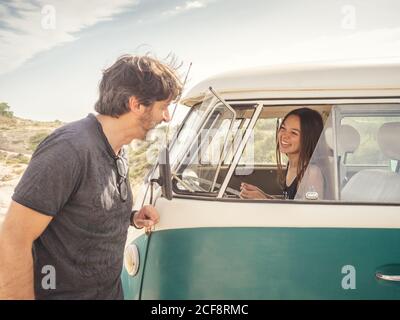 Side view of kind smiling man talking to pretty Woman laughing in front seat of car in desert place Stock Photo