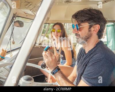 Bearded man and long haired Woman in colorful sunglasses sitting in front sea of car and looking at blue little toy car Stock Photo