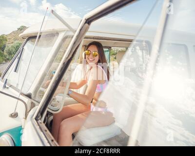 Cheerful young Woman smiling and looking at camera sitting at steering wheel of car in bright sunny day Stock Photo