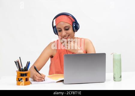 Pretty Indian woman at the table, distance learning for students. Freelancer, distant work, work at home, online education, Listening to music. Stock Photo