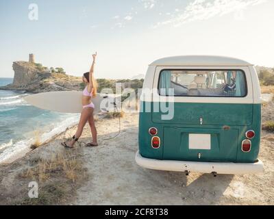 Charming long haired Woman going to surf holding surfboard near vintage van Stock Photo