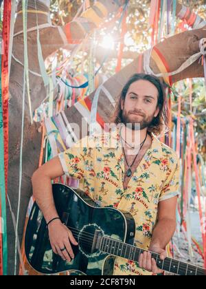 Bearded man sitting under decorated tree playing guitar Stock Photo