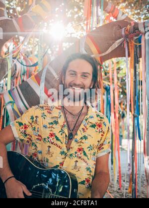 Bearded man sitting under decorated tree playing guitar Stock Photo