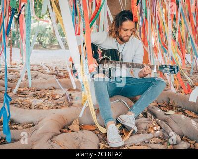 Bearded man sitting under decorated tree playing guitar Stock Photo