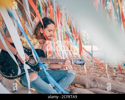 Bearded man sitting under decorated tree playing guitar Stock Photo