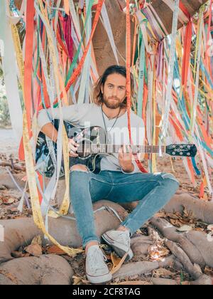 Bearded man sitting under decorated tree playing guitar Stock Photo