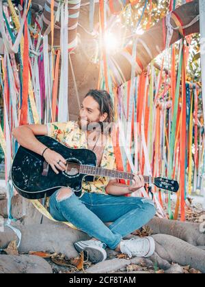 Bearded man sitting under decorated tree playing guitar Stock Photo