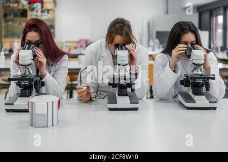 Women in white coats using modern microscopes to examine tissue cells during work in laboratory Stock Photo