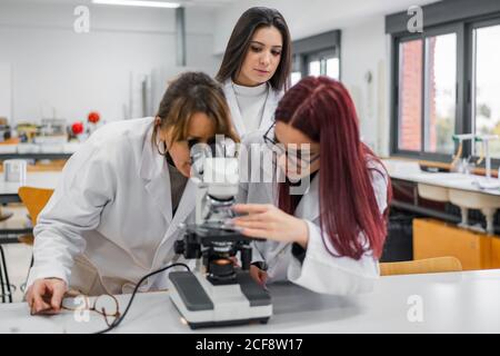 Woman using microscope near colleagues in laboratory Stock Photo
