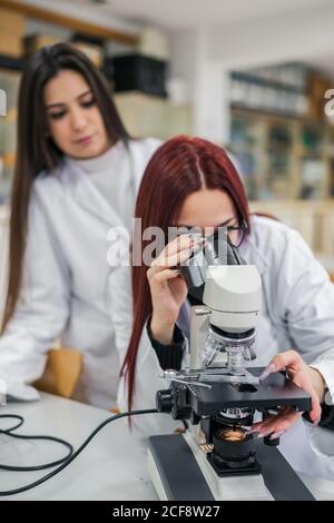 Woman using microscope near colleagues in laboratory Stock Photo