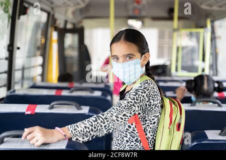 Portrait of Girl kid student in medical mask inside the school bus looking at camera - Concept of school reopen or back to school with new normal Stock Photo