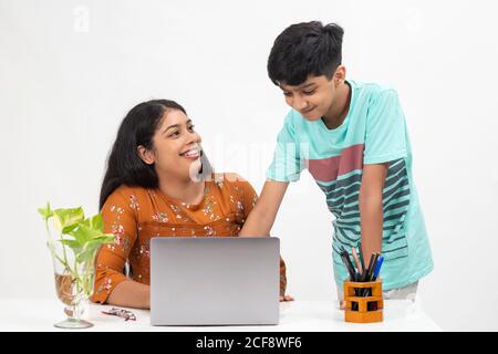 A boy points to a laptop as the girl sits on a table, distance learning for students, study from home, online education, Discussing project. Stock Photo
