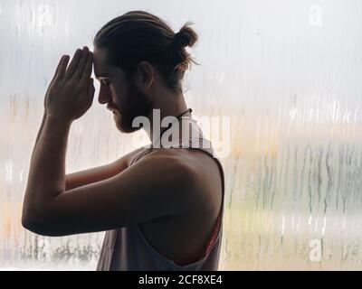 Relaxed thoughtful male in harmony with praying hands in forehead near steamy windows with closed eyes Stock Photo