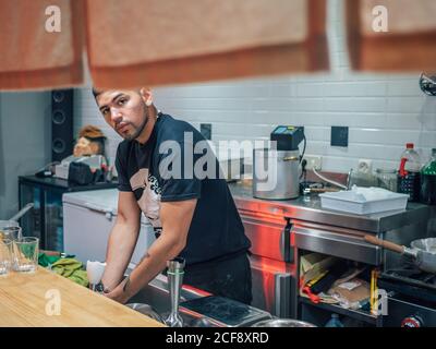 Handsome ethnic young man washing hands while working in Japanese restaurant and cooking ramen Stock Photo