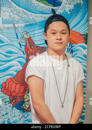 Young man in white t-shirt and black cap standing and looking at camera with painting of horse behind Stock Photo