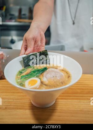 anonymous man putting bowls of fresh cooked traditional Japanese dish on wooden counter in restaurant Stock Photo