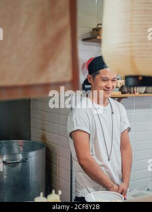 Young man standing with hands in pockets while cooking Japanese dish ramen in restaurant Stock Photo
