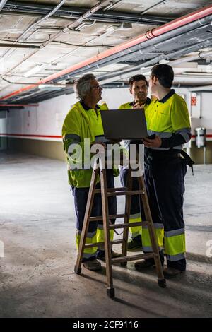 Group of skilled male engineers in uniform using gadgets while examining electrical equipment in modern building Stock Photo