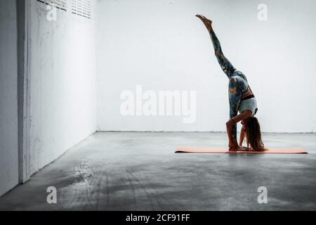 Side view of flexible female in active wear standing on mat and doing yoga in Urdhva Prasarita Eka Padasana and balancing Stock Photo