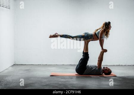 Side view of adult couple doing pair yoga in Front Bird pose on mat and holding hands Stock Photo
