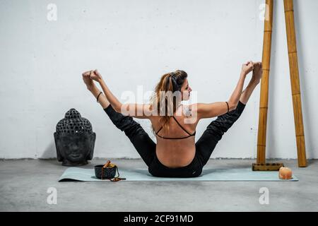 Serene female in sportswear sitting on mat in living room and