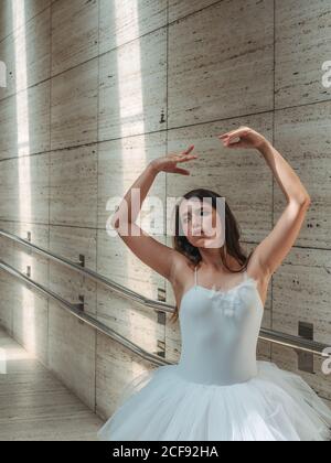 Ballerina in white ballet tutu performing exercises at rail in contrast sunny light Stock Photo