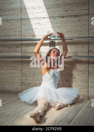 Ballerina sitting on floor stretching graceful leg in classroom Stock Photo