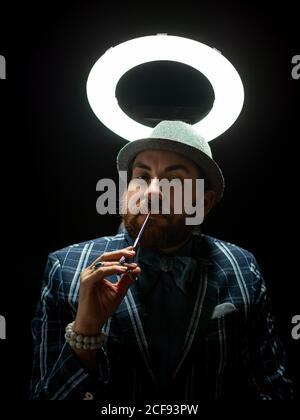 Stylish bearded man with scissors thoughtfully planning haircut on black background under white light on black background Stock Photo