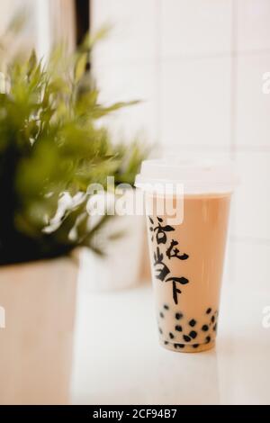 Tasty milk bubble tea with tapioca pearls in plastic cup on table near potted plants in traditional Taiwanese cafe Stock Photo