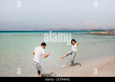 Playful man and Woman in white shirts playing in shallow water of seashore in summer Stock Photo