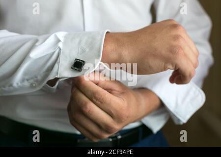 The groom fastens the button of the cufflink on the shirt sleeve Stock Photo