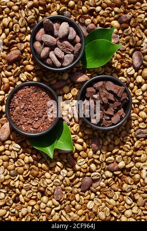 Flat lay  of clay bowl with Raw cocoa beans,  cocoa powder, chocolate on sacking  on coffee beans  as background, top view Stock Photo