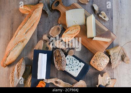 From above delightful various types of white cheese and crispy fresh bread with pieces of wood on rustic table Stock Photo