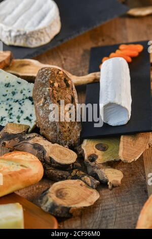 Delightful various types of white cheese and crispy fresh bread with pieces of wood on rustic table Stock Photo