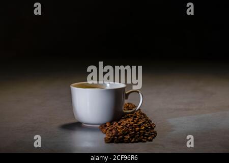 Fresh black coffee in white ceramic cup placed on saucer near coffee grinder and coffee beans on concrete table Stock Photo