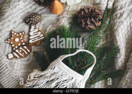 Zero waste christmas holidays. Reusable shopping bag with green spruce branches, gingerbread christmas cookies and pine cones on white knitted sweater Stock Photo