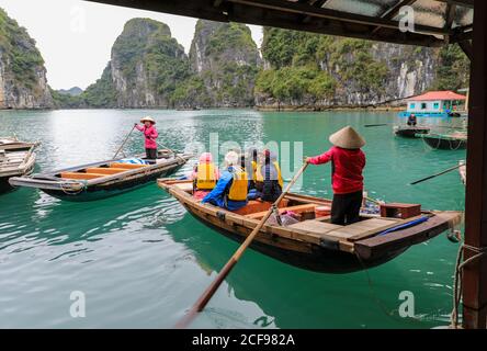 A woman wearing a traditional Vietnamese conical hat called a nón lá, rowing a boat full of tourists at Hạ Long Bay, Vietnam, Asia Stock Photo