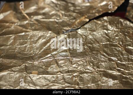 Crumpled and torn golden bronze shiny foil texture background Stock Photo