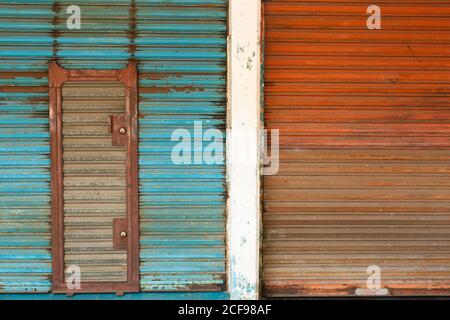 Weathered rusty metal shutter doors painted in blue and red color with shut doorway Stock Photo