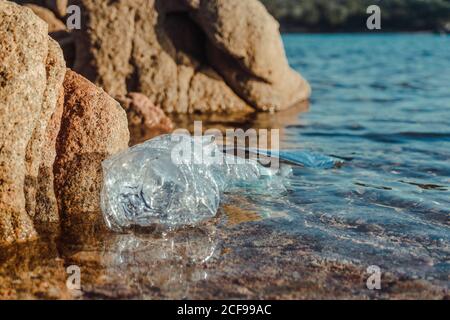 Empty plastic crumpled bottles waste lying in clear water on seaside near rocks Stock Photo